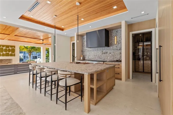 Kitchen featuring wooden ceiling, a raised ceiling, decorative backsplash, light stone countertops, and a large island with sink