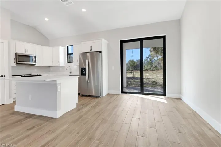 Kitchen with light hardwood / wood-style flooring, appliances with stainless steel finishes, white cabinetry, a wealth of natural light, and a kitchen island