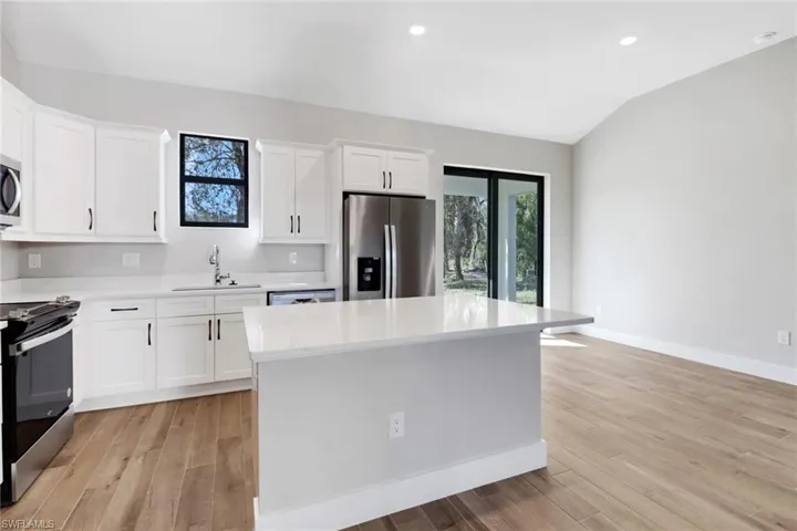 Kitchen with lofted ceiling, sink, white cabinetry, stainless steel appliances, and a center island