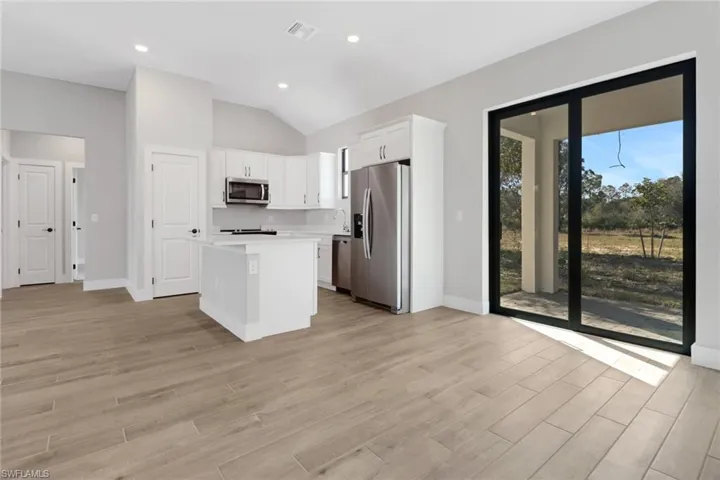 Kitchen featuring light wood-style flooring, appliances with stainless steel finishes, white cabinets, a kitchen island, and tall ceiling