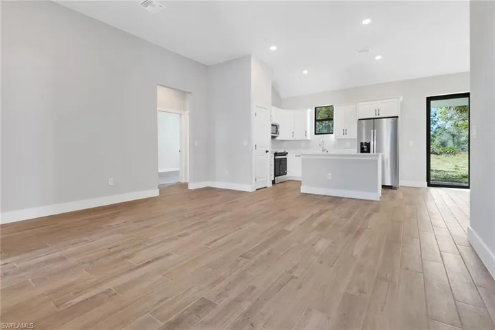 Unfurnished living room featuring high vaulted ceiling, sink, and light hardwood / wood-style floors