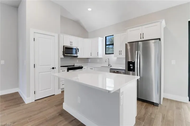 Kitchen with a kitchen island, appliances with stainless steel finishes, white cabinetry, sink, and light wood-type flooring