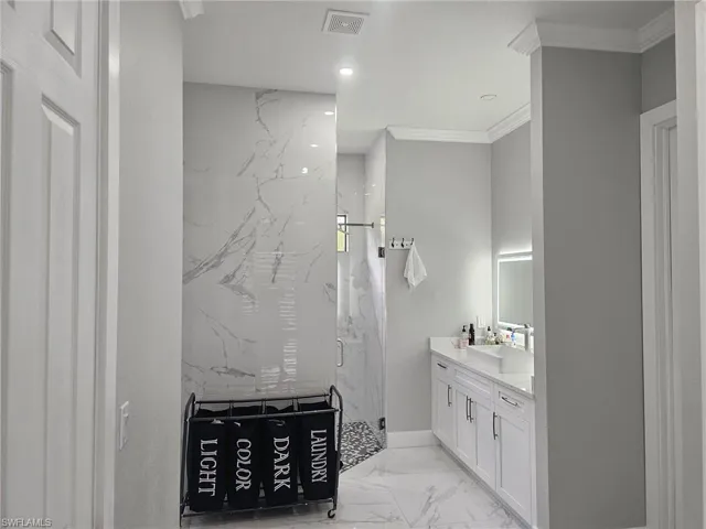 Bathroom featuring vanity, ornamental molding, and a tile shower