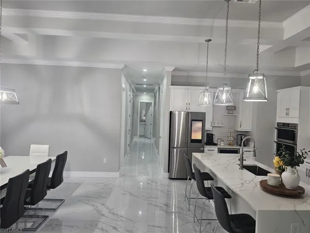 Kitchen featuring pendant lighting, crown molding, sink, appliances with stainless steel finishes, and white cabinets