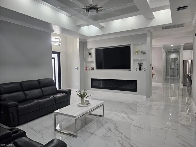 Living room with ornamental molding, coffered ceiling, built in features, and ceiling fan