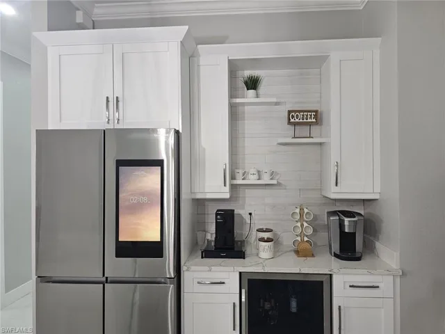 Kitchen with stainless steel refrigerator with ice dispenser, beverage cooler, light stone counters, and white cabinets