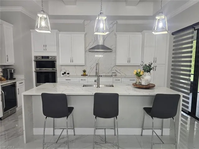 Kitchen with white cabinets, beverage cooler, an island with sink, and light stone countertops