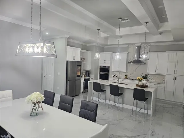Kitchen with hanging light fixtures, stainless steel appliances, a large island with sink, wall chimney range hood, and a breakfast bar