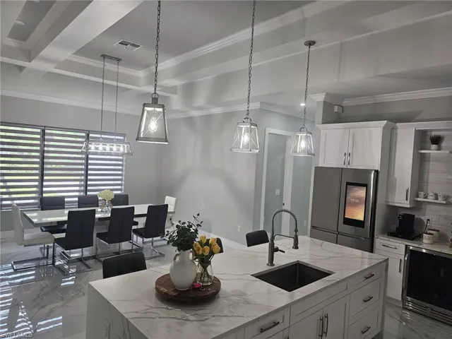 Kitchen featuring pendant lighting, stainless steel refrigerator, white cabinetry, sink, and a center island with sink
