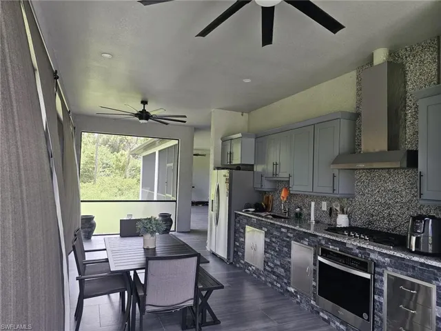 Kitchen featuring backsplash, stainless steel appliances, gray cabinets, wall chimney exhaust hood, and ceiling fan