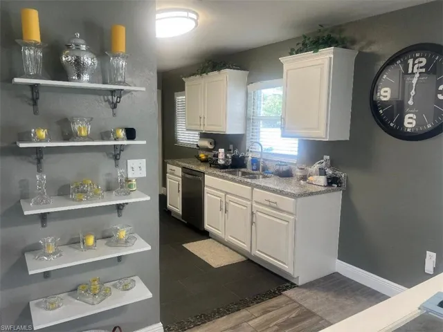 Kitchen with stainless steel dishwasher, sink, light stone countertops, and white cabinetry