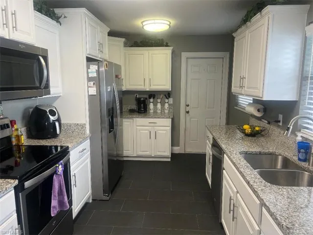 Kitchen featuring appliances with stainless steel finishes, white cabinets, sink, light stone counters, and dark tile patterned flooring