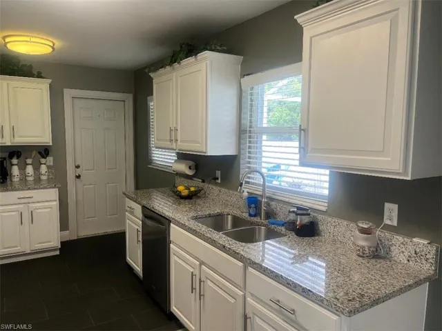 Kitchen with white cabinets, sink, dark tile patterned flooring, light stone countertops, and dishwasher