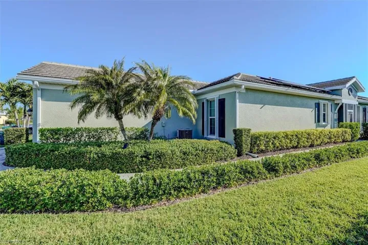 View of side of home with roof mounted solar panels, stucco siding, cooling unit, and a lawn