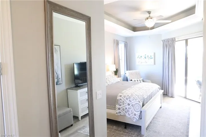 Bedroom with ceiling fan, light wood-type flooring, access to outside, and a tray ceiling
