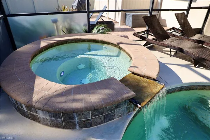 View of swimming pool with pool water feature, glass enclosure, a patio area, and an in ground hot tub