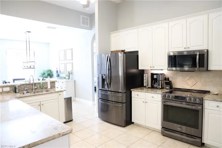 Kitchen with white cabinets, light tile patterned flooring, decorative light fixtures, and appliances with stainless steel finishes