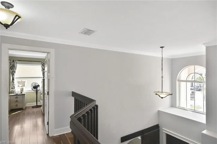 Hall featuring dark wood-style floors, ornamental molding, and an upstairs landing