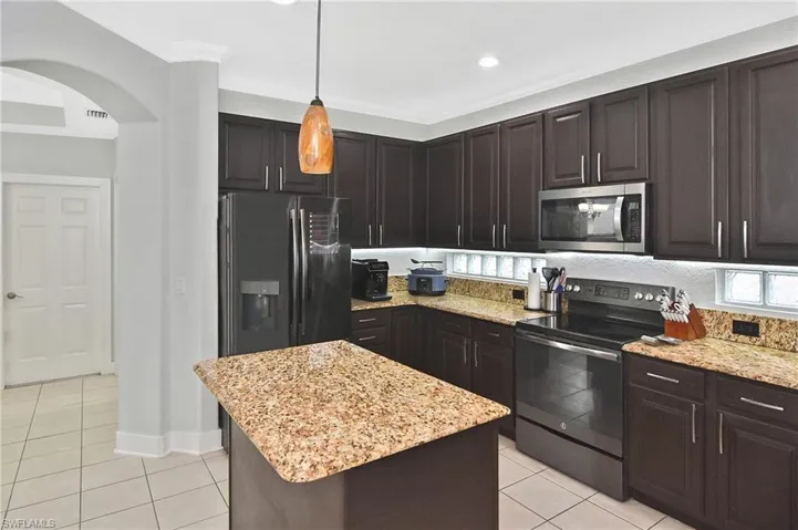 Kitchen featuring range with electric cooktop, dark wood finish cabinetry, stainless steel microwave, and light tile patterned floors