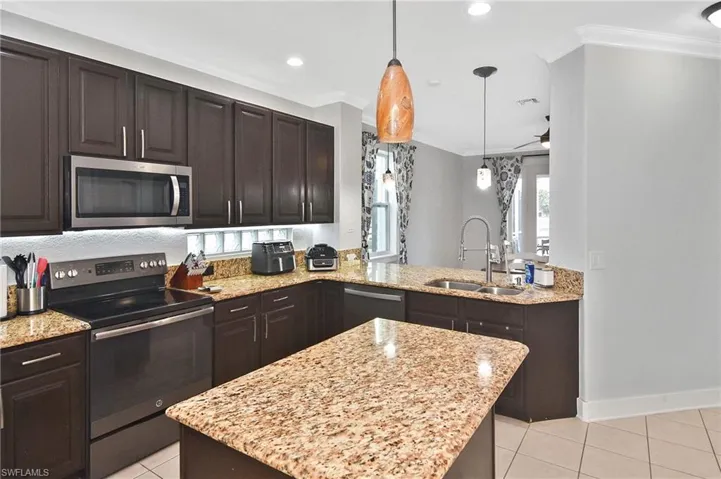 Kitchen featuring stainless steel appliances, dark wood finish cabinets, light stone countertops, crown molding, and decorative light fixtures