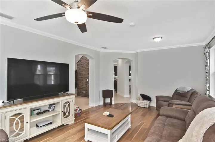 Living area featuring crown molding, arched walkways, light wood-style floors, and a ceiling fan