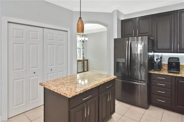 Kitchen with stainless steel fridge with ice dispenser, hanging light fixtures, a center island, light stone countertops, and crown molding