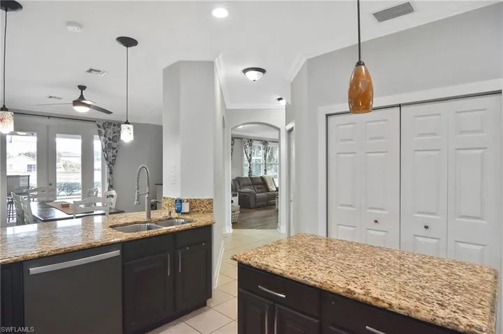 Kitchen with pendant lighting, ceiling fan, dishwasher, light stone counters, and ornamental molding