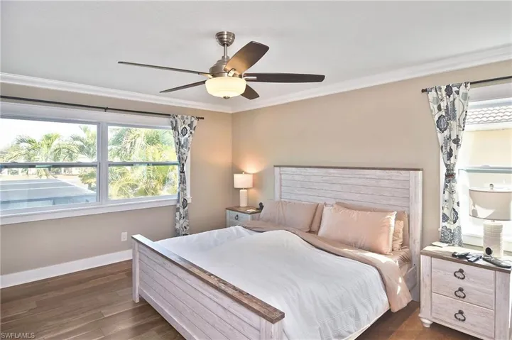 Bedroom with dark wood-style flooring, ceiling fan, and ornamental molding