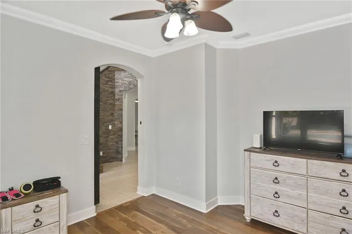 Bedroom featuring arched walkways, crown molding, dark wood-style floors, and a ceiling fan