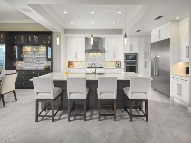 Kitchen featuring wall chimney exhaust hood, built in appliances, and an island with sink