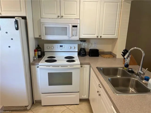 Kitchen featuring white appliances, white cabinets, light tile patterned floors, and light countertops