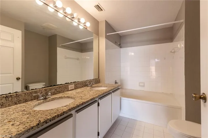 Bathroom with toilet, shower / bath combination, double vanity, and tile patterned flooring