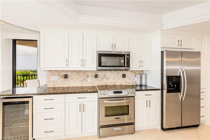 Kitchen with white cabinets, crown molding, appliances with stainless steel finishes, dark stone counters, and wine cooler