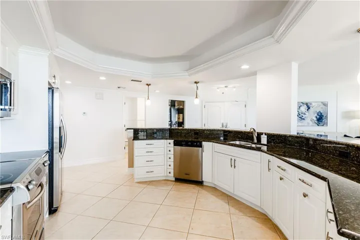 Kitchen with pendant lighting, dark stone counters, white cabinetry, stainless steel appliances, and sink
