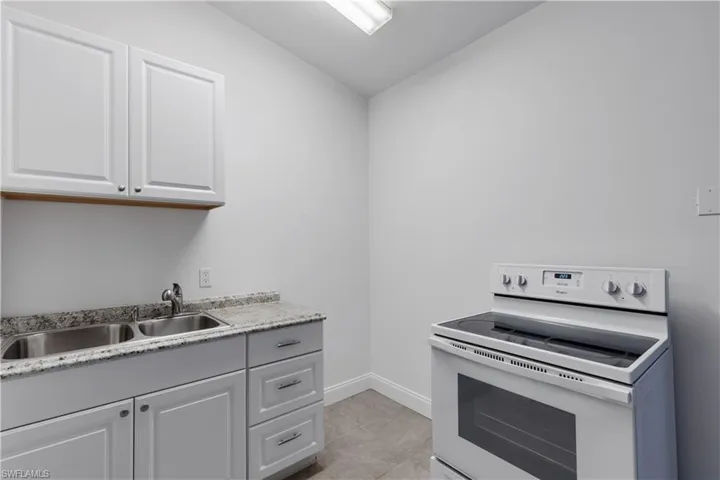 Kitchen with white cabinetry, light tile patterned flooring, white electric range oven, lofted ceiling, and sink