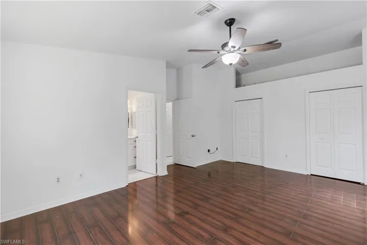 Unfurnished bedroom featuring dark hardwood / wood-style flooring, ceiling fan, ensuite bath, and multiple closets