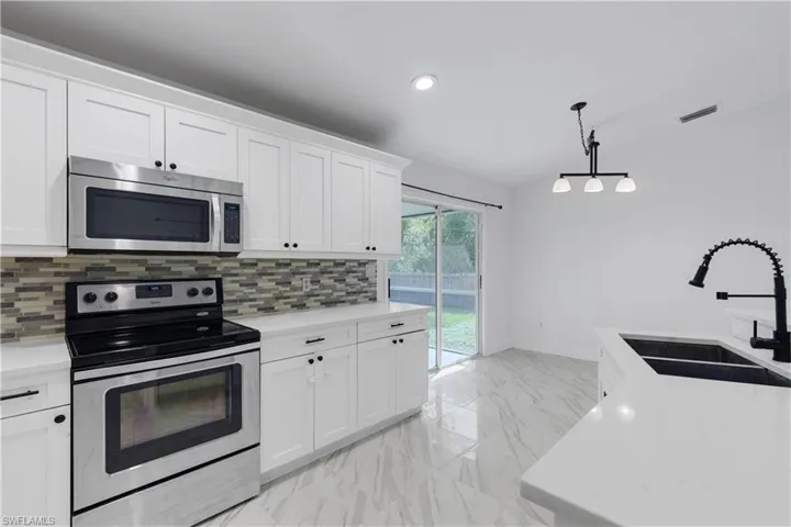 Kitchen featuring pendant lighting, sink, white cabinetry, stainless steel appliances, and backsplash