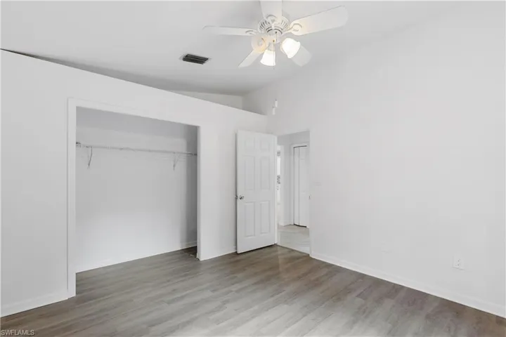 Unfurnished bedroom with vaulted ceiling, ceiling fan, a closet, and hardwood / wood-style flooring