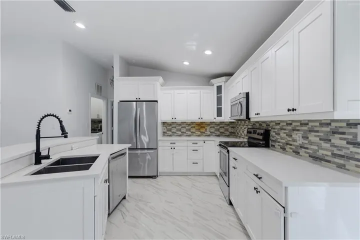 Kitchen with lofted ceiling, sink, backsplash, white cabinetry, and stainless steel appliances