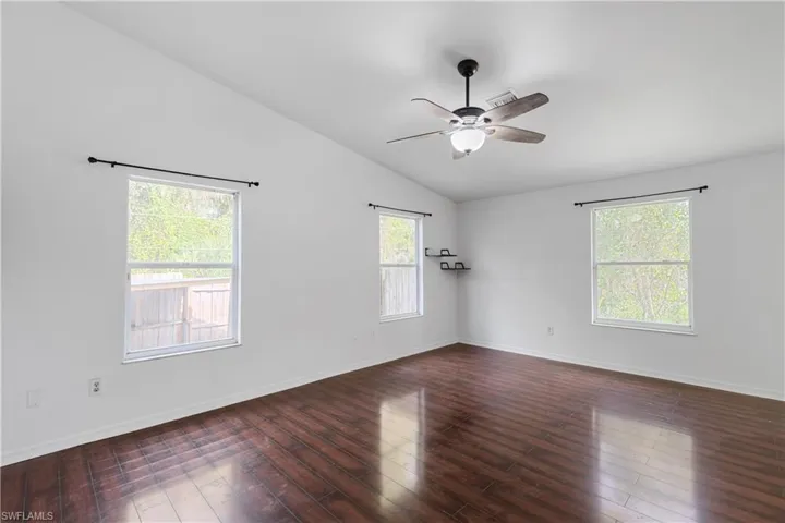 Spare room with lofted ceiling, dark hardwood / wood-style flooring, ceiling fan, and a wealth of natural light