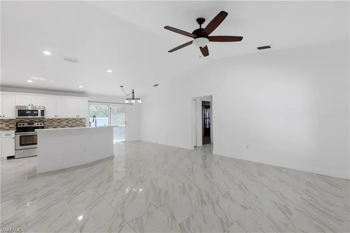 Unfurnished living room with vaulted ceiling, sink, and ceiling fan