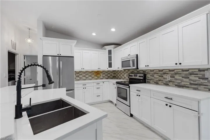 Kitchen with appliances with stainless steel finishes, hanging light fixtures, tasteful backsplash, white cabinets, and lofted ceiling