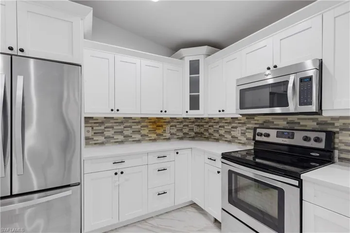 Kitchen with white cabinets, stainless steel appliances, tasteful backsplash, and lofted ceiling