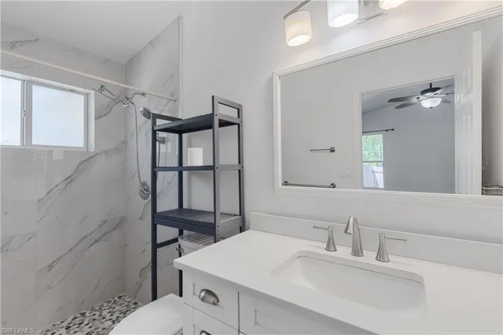 Bathroom featuring tiled shower, vanity, toilet, and ceiling fan