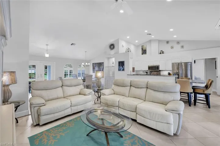 Living room with light tile patterned floors, ceiling fan with notable chandelier, and high vaulted ceiling