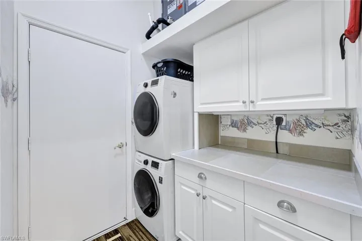 Laundry room featuring cabinets, stacked washer / dryer, and dark wood-type flooring