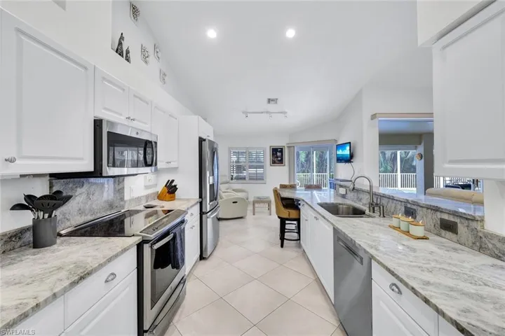 Kitchen with appliances with stainless steel finishes, white cabinetry, vaulted ceiling, and sink