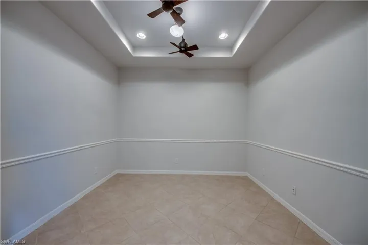 Tiled empty room featuring ceiling fan and a raised ceiling