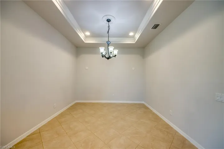 Tiled empty room featuring a raised ceiling and an inviting chandelier