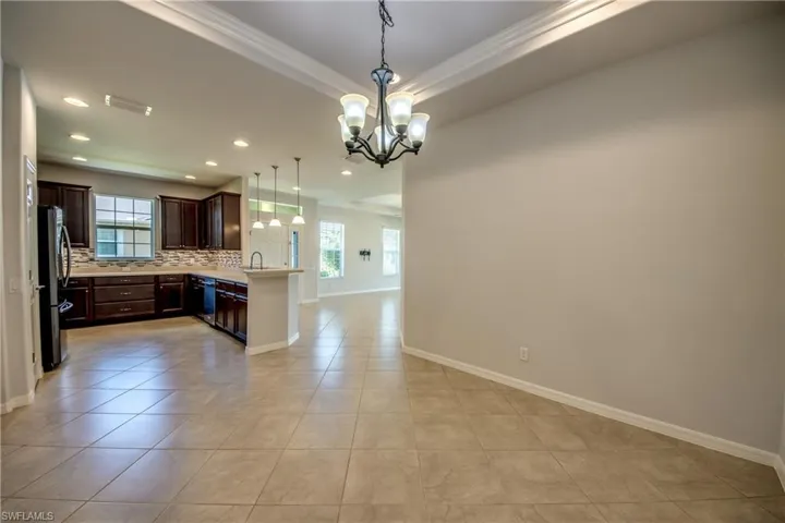 Kitchen featuring dark brown cabinets, light tile patterned flooring, stainless steel refrigerator, decorative backsplash, and kitchen peninsula